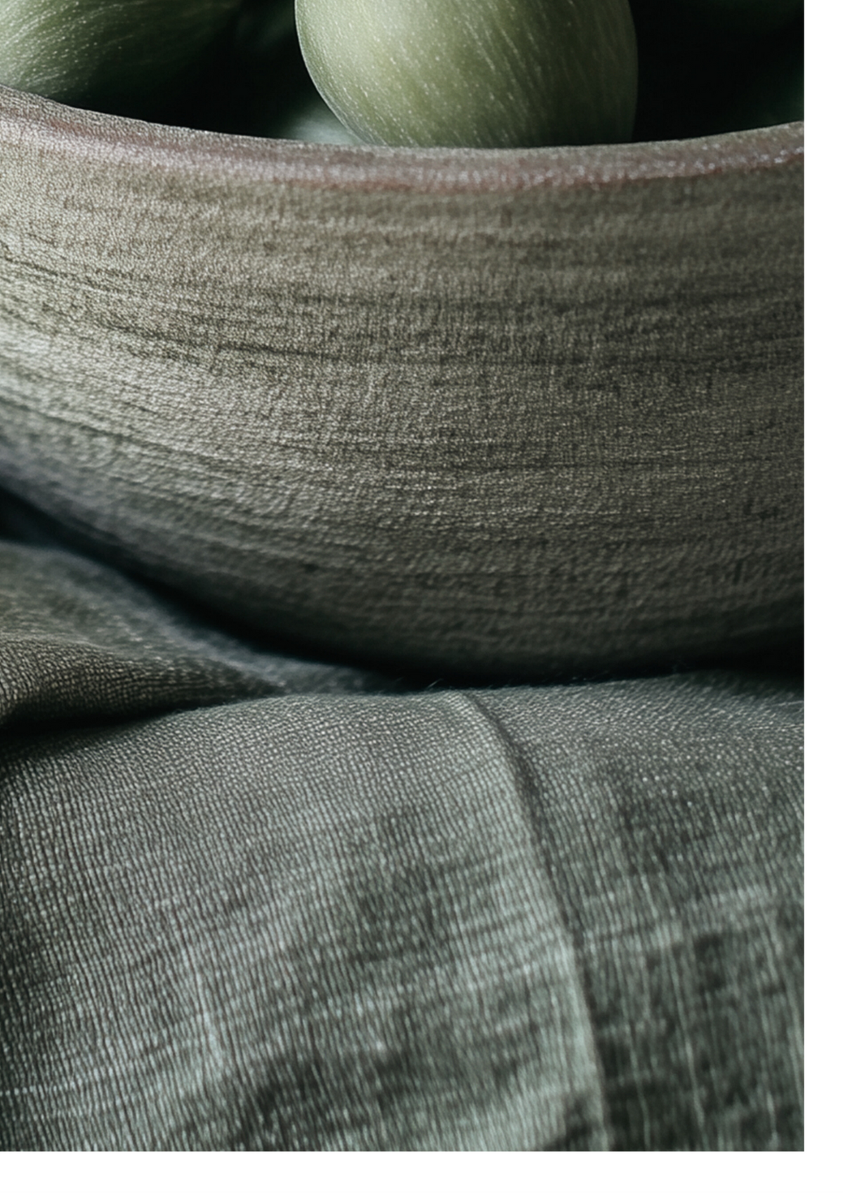 Close-up of a textured gray fabric surface with a matching gray bowl holding muted green round objects.