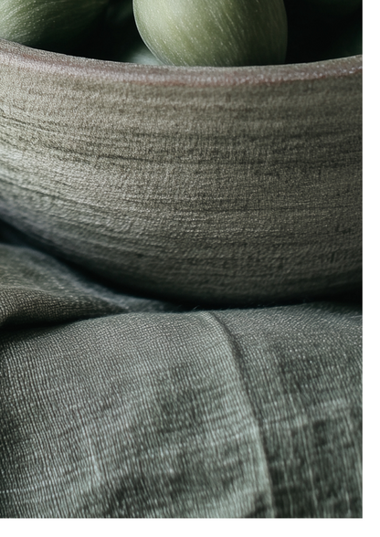 Close-up of a textured gray fabric surface with a matching gray bowl holding muted green round objects.