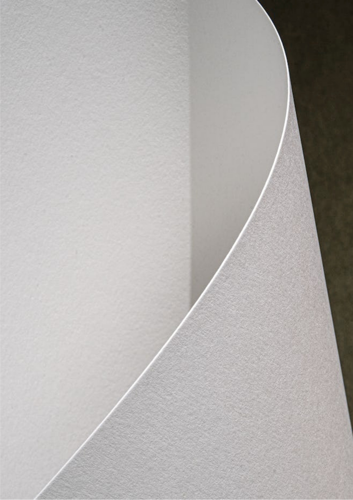 A close-up of a textured white sheet of paper or vinyl, curled over to show its matte surface and edge against a dark background.