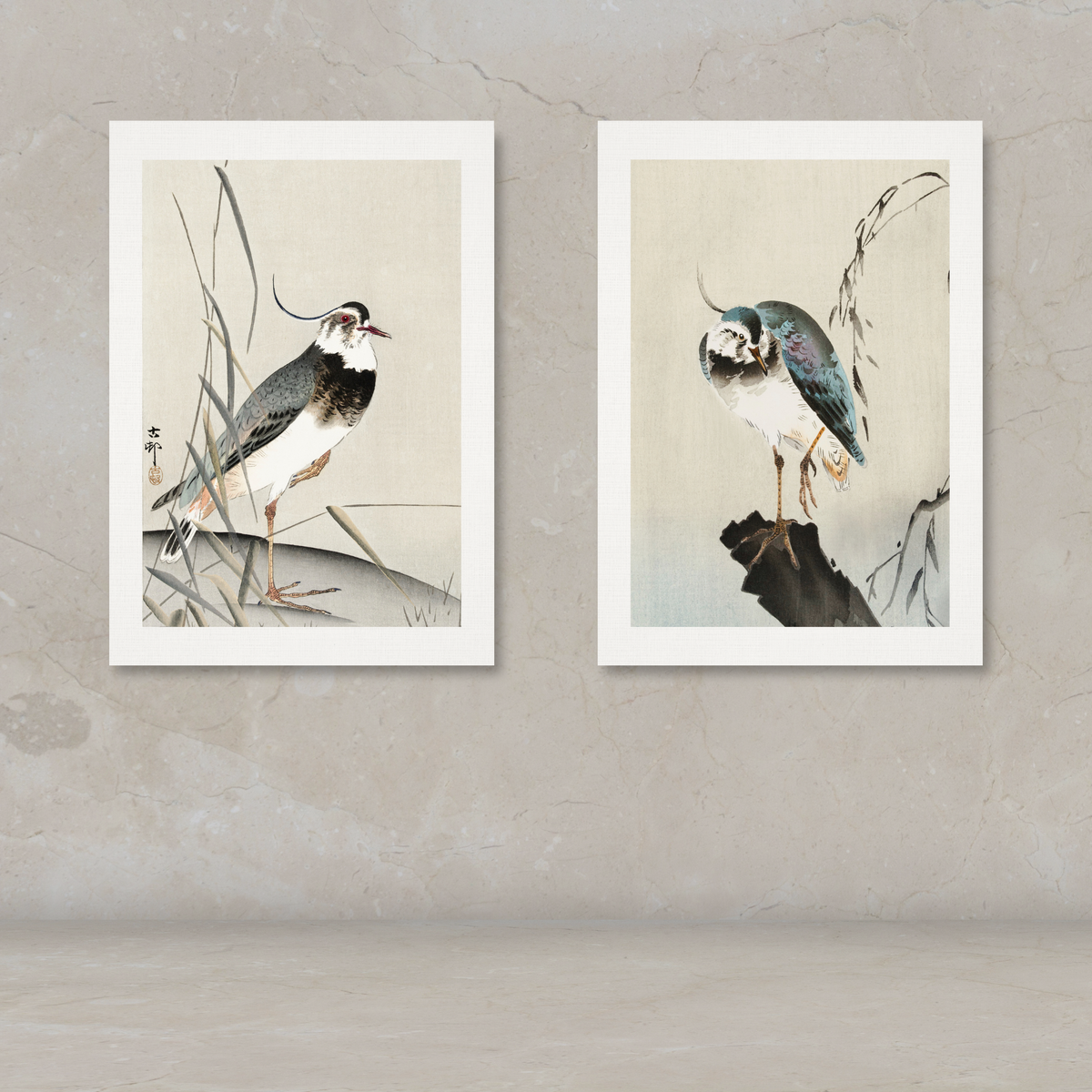 Two framed vertical art prints depicting birds in a traditional Japanese style, displayed side-by-side on a textured beige wall above a matching surface.