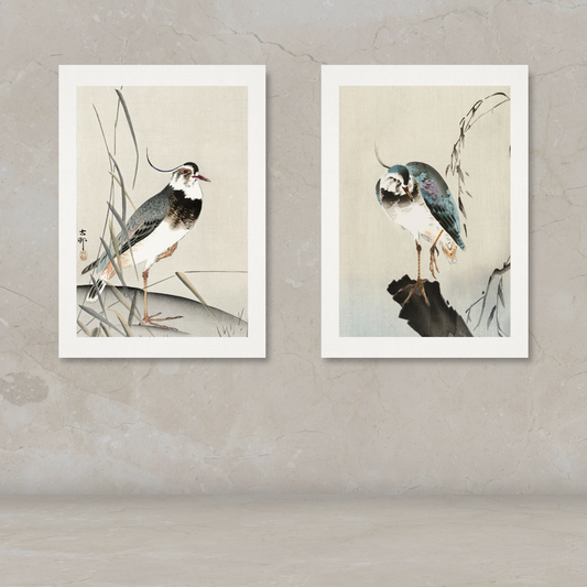 Two framed vertical art prints depicting birds in a traditional Japanese style, displayed side-by-side on a textured beige wall above a matching surface.