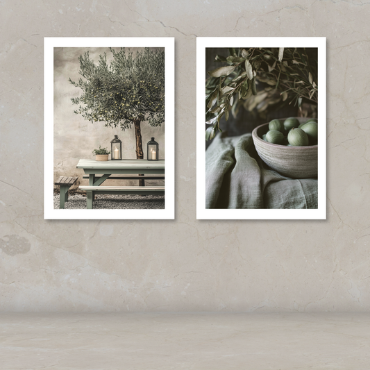 Two framed art prints with white borders displayed side-by-side on a textured beige wall. The left print shows an olive tree on a bench with lanterns, and the right print shows green olives in a bowl with olive branches.
