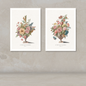 Two framed botanical art prints of flower bouquets in urns, displayed side by side on a textured beige wall above a light floor.